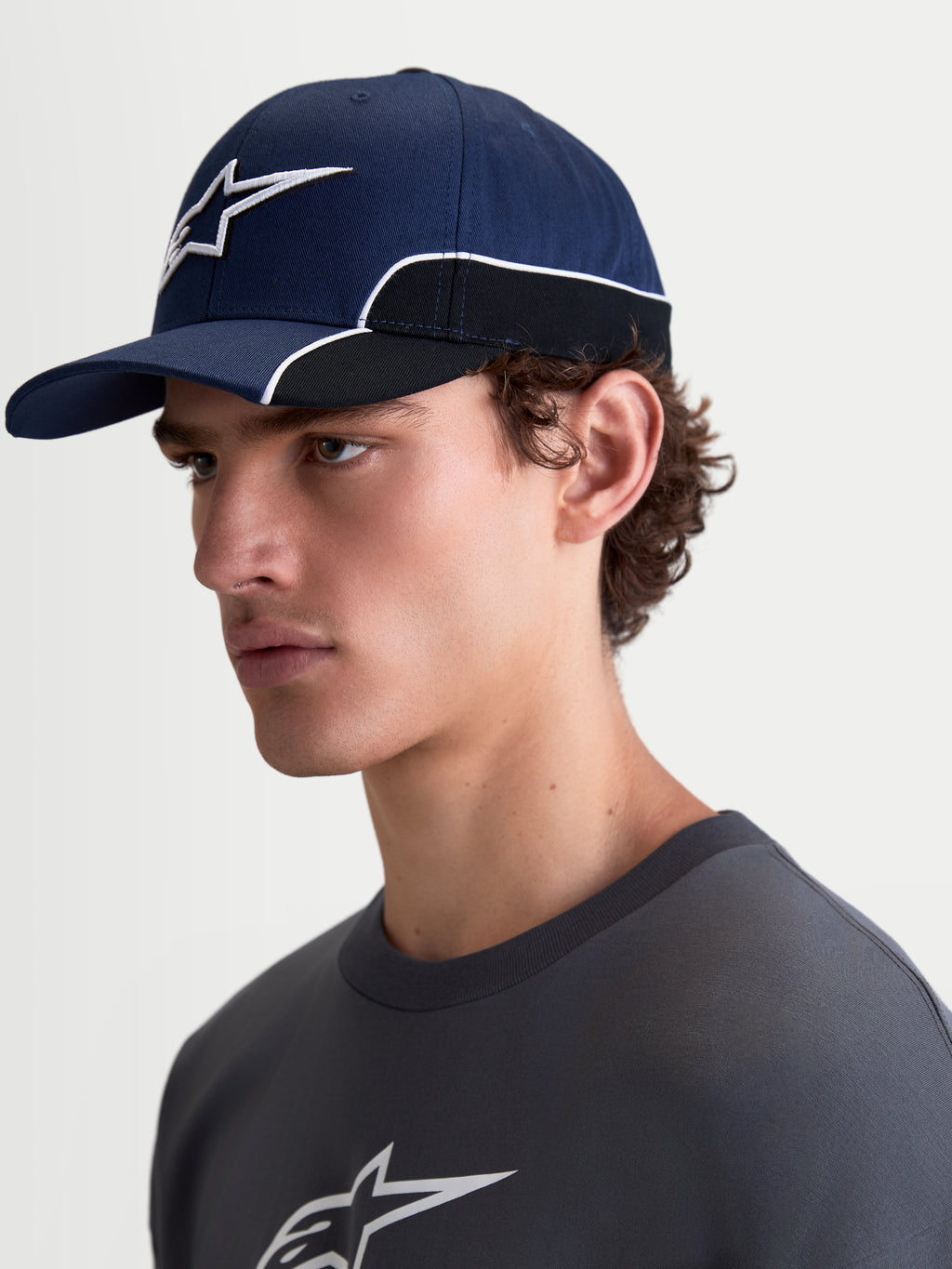 Alpinestars 500 Snapback pet, sportswearpet, unisex, blauw en zwart, duurzaam katoen, voorzien van een gebogen klep en 3D Astars-logo borduursel met witte contrastbiezen, zijaanzicht op model.