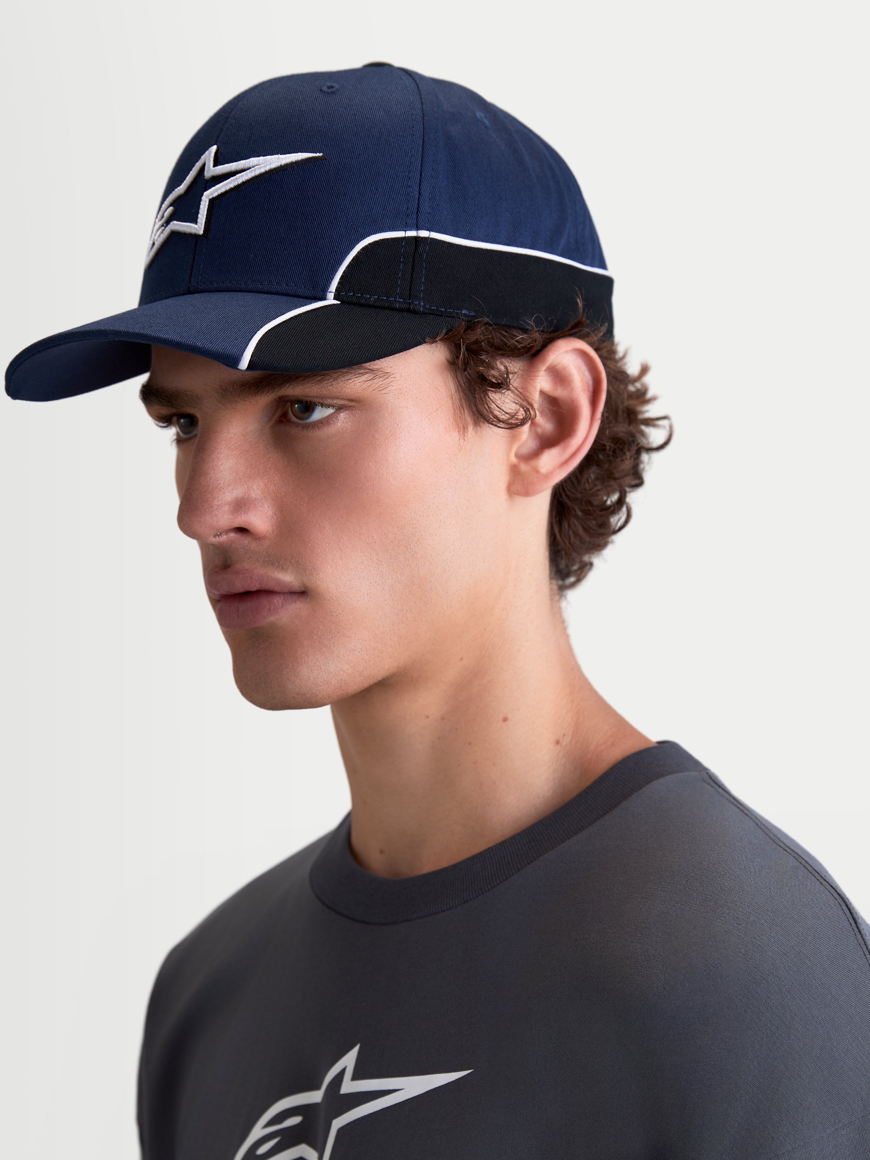 Alpinestars 500 Snapback pet, sportswearpet, unisex, blauw en zwart, duurzaam katoen, voorzien van een gebogen klep en 3D Astars-logo borduursel met witte contrastbiezen, zijaanzicht op model.