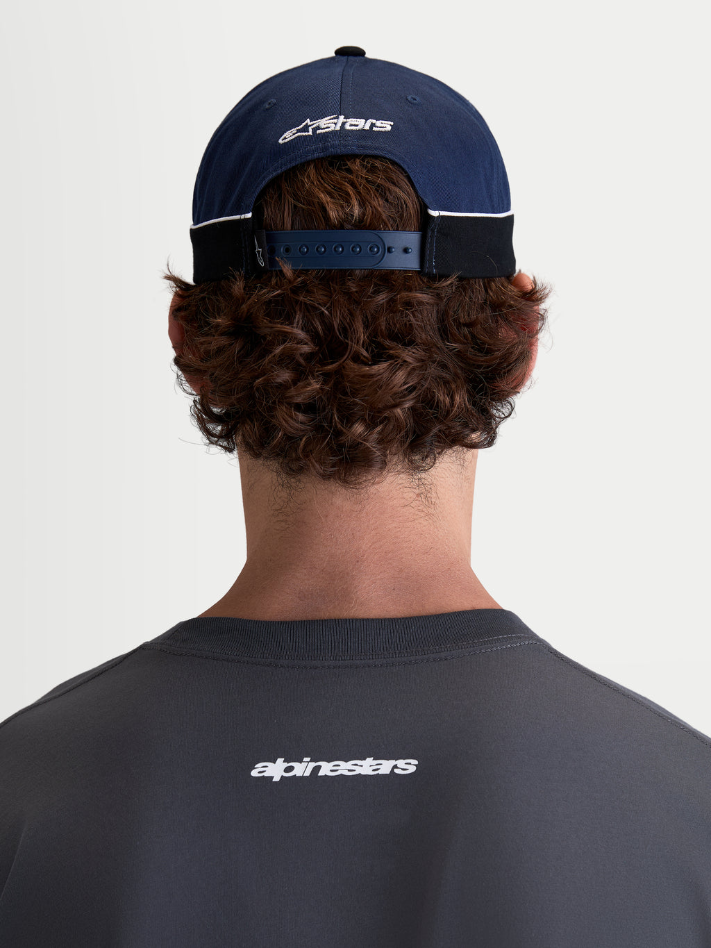 Alpinestars 500 Snapback pet, motorsport-ge''nspireerde sportswear pet, marineblauw en zwart, 100% katoenen keperstof met een verstelbare snapbacksluiting en geborduurd Astars-logo, achteraanzicht op model.
