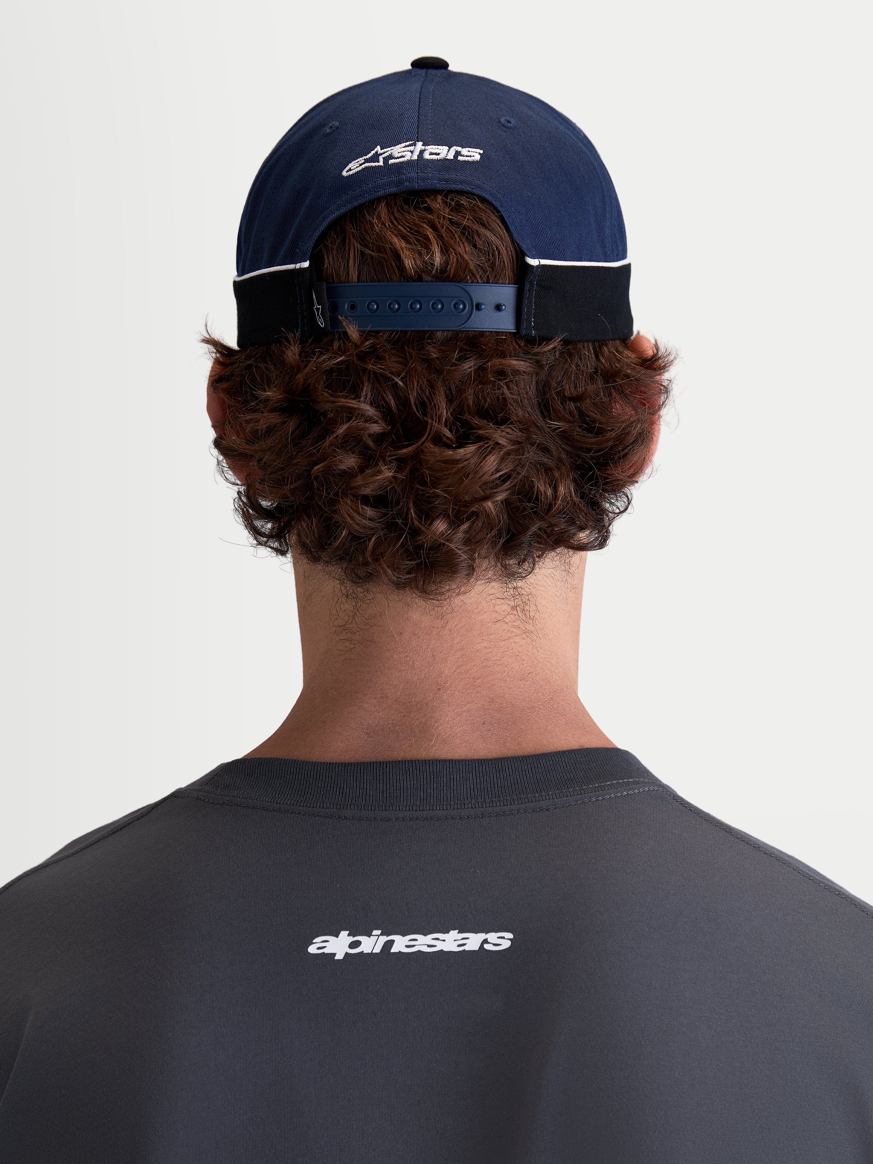 Alpinestars 500 Snapback pet, motorsport-ge''nspireerde sportswear pet, marineblauw en zwart, 100% katoenen keperstof met een verstelbare snapbacksluiting en geborduurd Astars-logo, achteraanzicht op model.