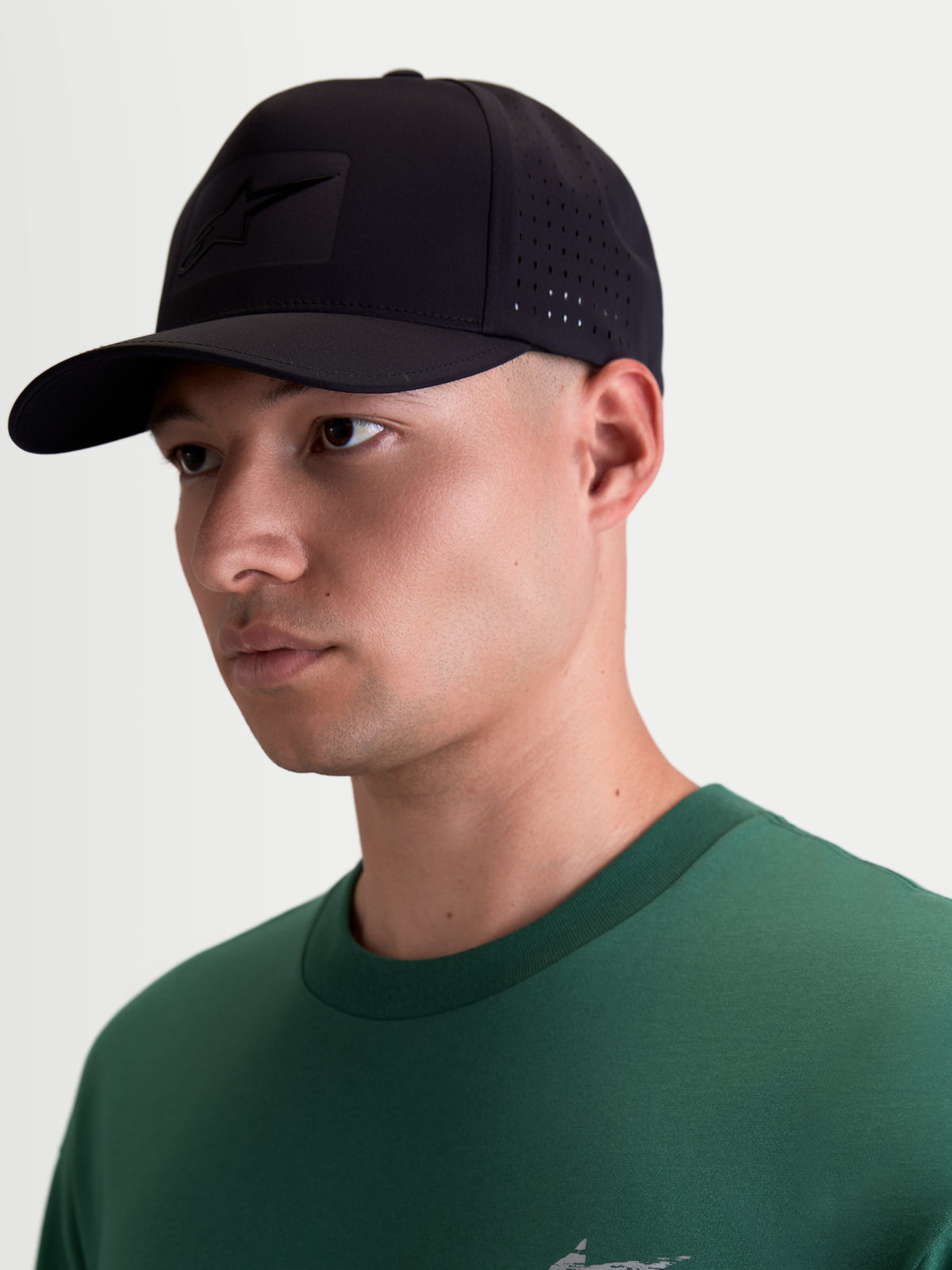Alpinestars Algo Perf Adjustable Hat, on-model view of a black motorsport-inspired sportswear cap featuring a curved bill, technical fabric with side perforations for ventilation, and a tonal sonic-weld Astars logo.