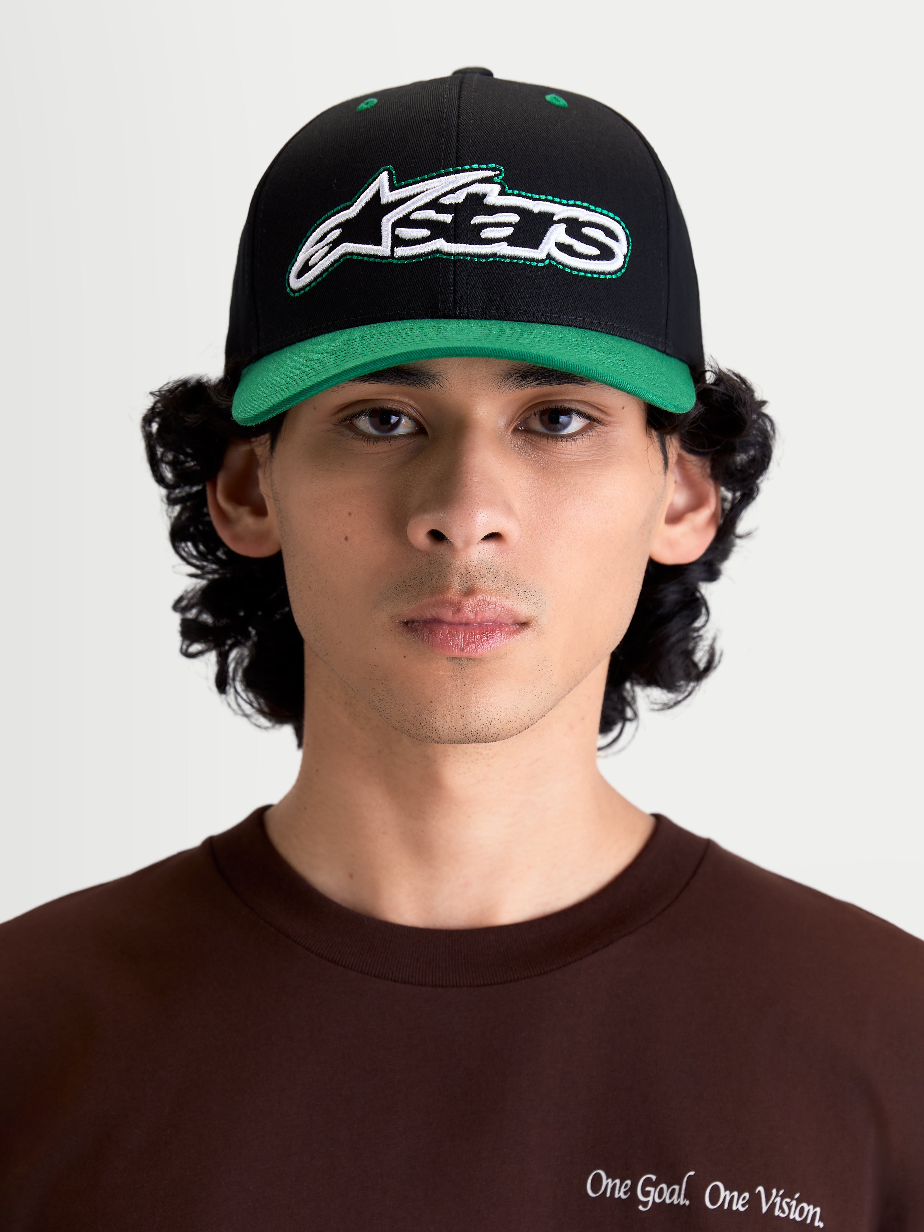 Alpinestars Retro Snapback pet, sportswear lifestyle-pet, zwart en groen, voorzien van een gebogen klep, gestructureerde kroon en geborduurd Astars-logo met groen contraststiksel op de voorzijde, getoond op model in vooraanzicht.