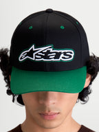 Alpinestars Retro Snapback pet, motorsport-geïnspireerde sportswear baseballpet met gebogen klep en gestructureerde kroon, unisex, zwart en groen, katoenen keperstof, vooraanzicht op model met het Astars-logo en groene contraststiksels.
