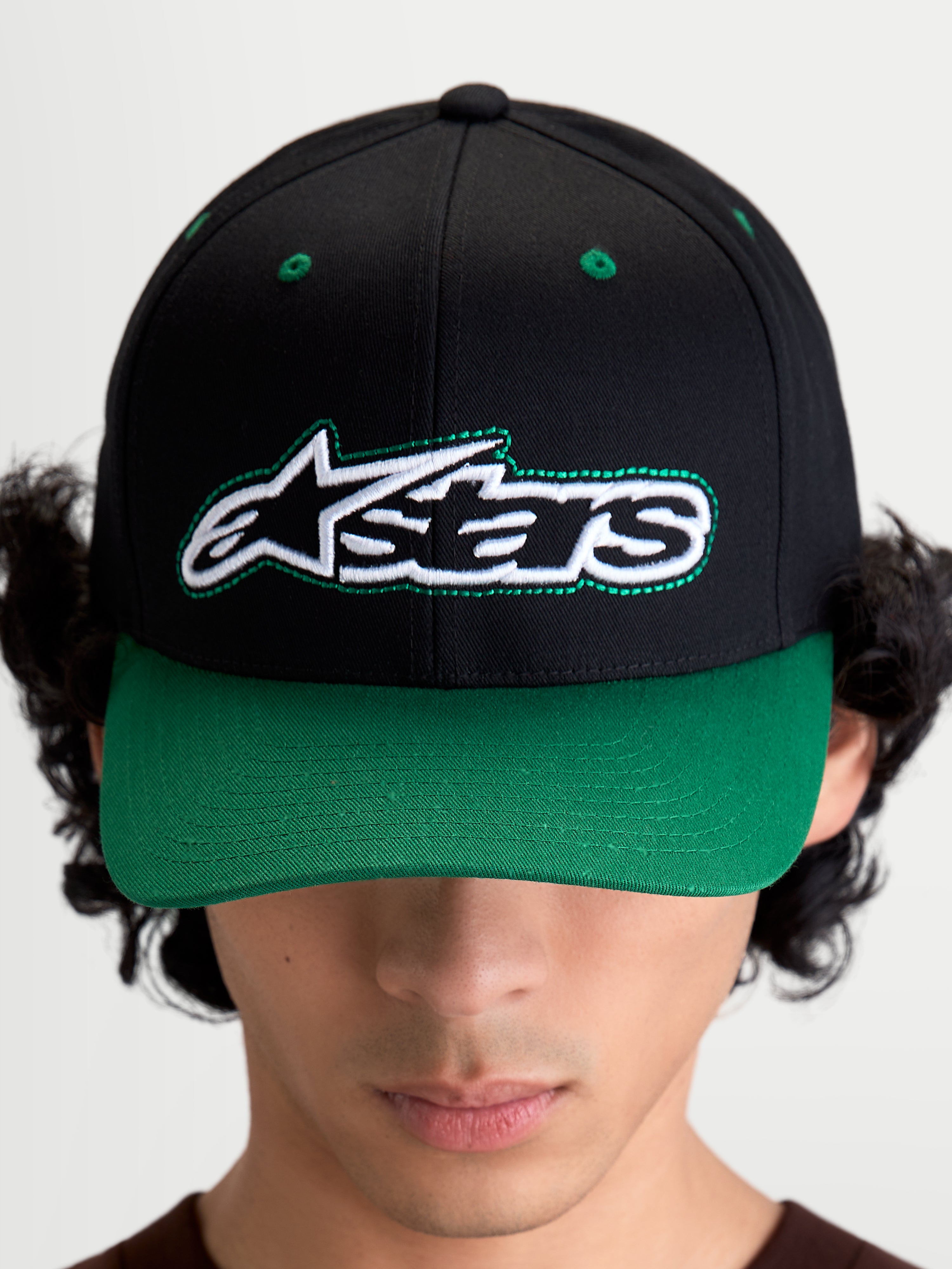 Alpinestars Retro Snapback pet, motorsport-geïnspireerde sportswear baseballpet met gebogen klep en gestructureerde kroon, unisex, zwart en groen, katoenen keperstof, vooraanzicht op model met het Astars-logo en groene contraststiksels.