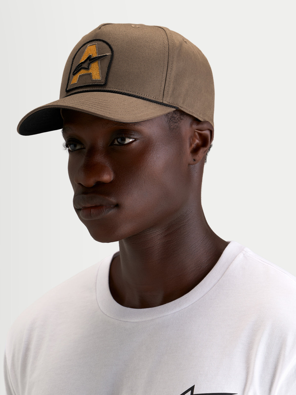 Alpinestars Acme Snapback Pet, casual sportswear pet in walnotebruin met gebogen klep en Astars-logoborduurpatch met koorddetail, gedragen door een model