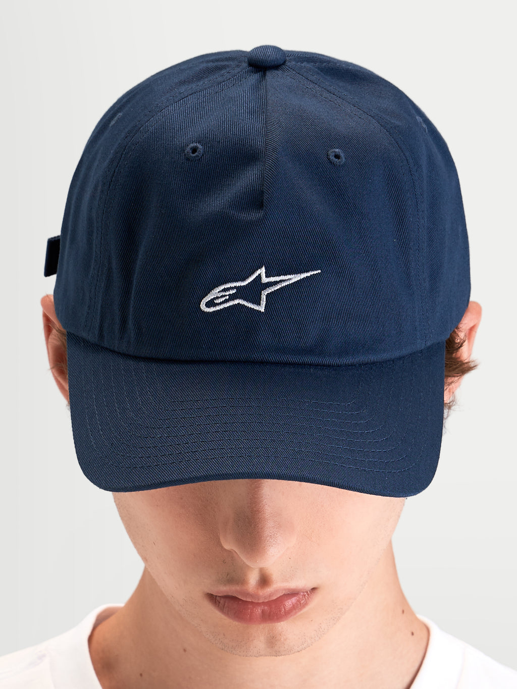 Alpinestars Casquette Dad Dylan, casquette sportswear décontractée bleue portée par un modèle, en sergé de coton avec visière courbée et logo Astars brodé en blanc à l'avant