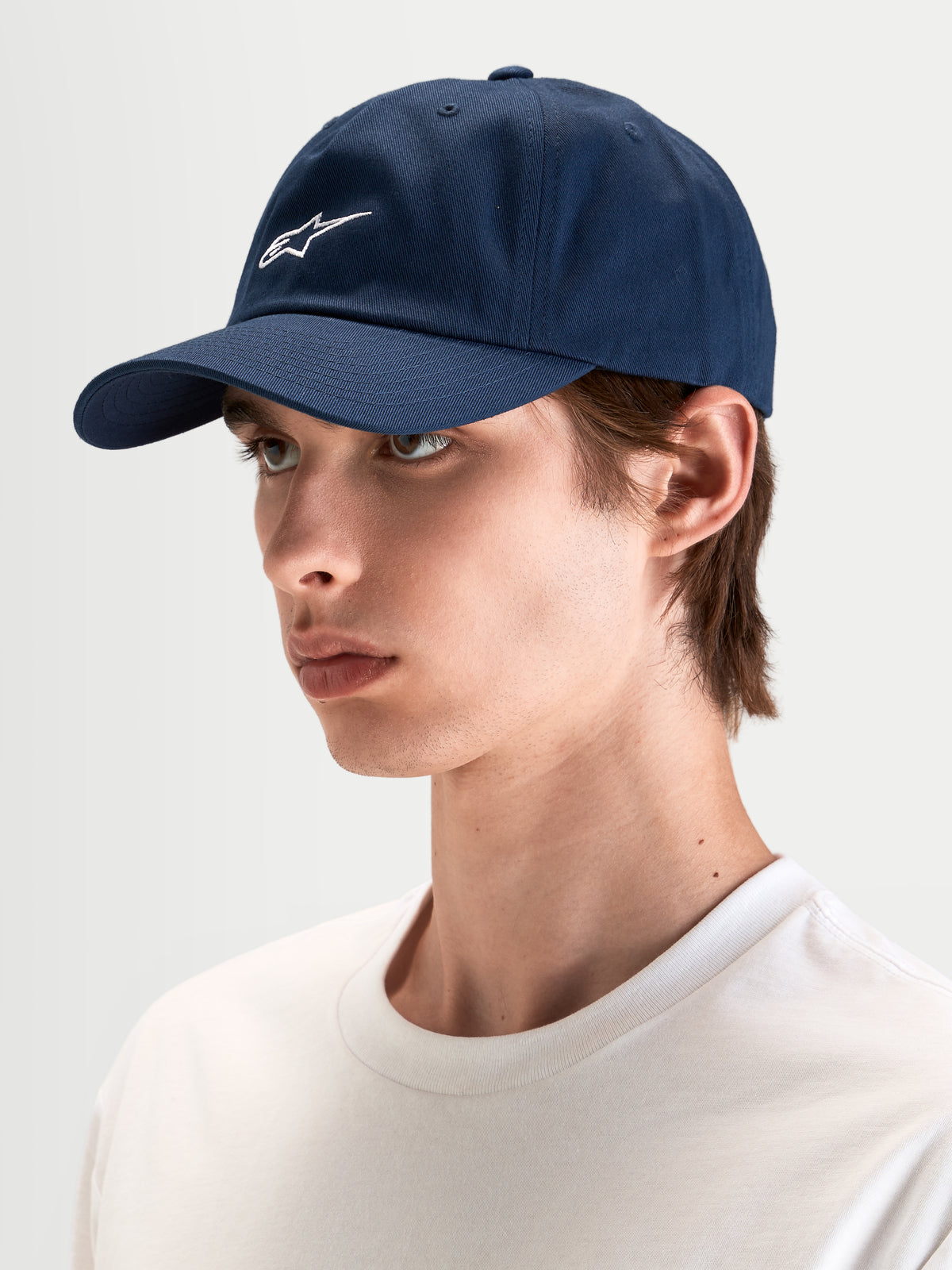 Casquette Dad Dylan d'Alpinestars, casquette sportswear décontractée bleu marine, portée par un modèle, avec visière courbée et broderie blanche du logo Astars sur l'avant