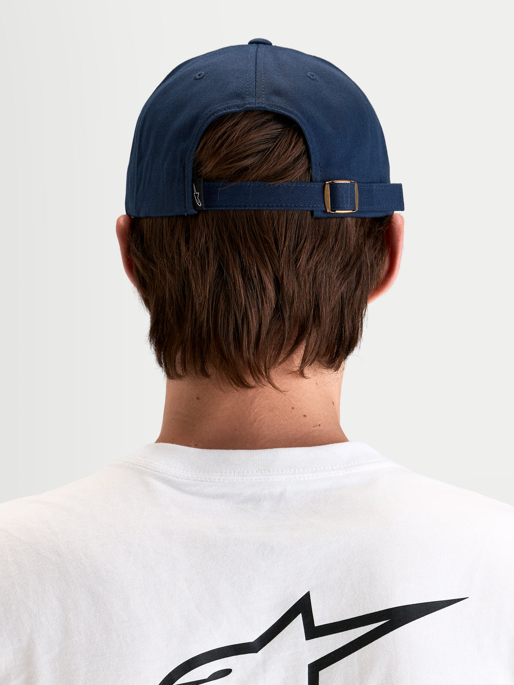 Alpinestars Casquette Dad Dylan, casquette sportswear décontractée en bleu marine, vue de dos montrant la sangle arrière réglable avec boucle en métal et petite étiquette du logo Astars portée par un modèle