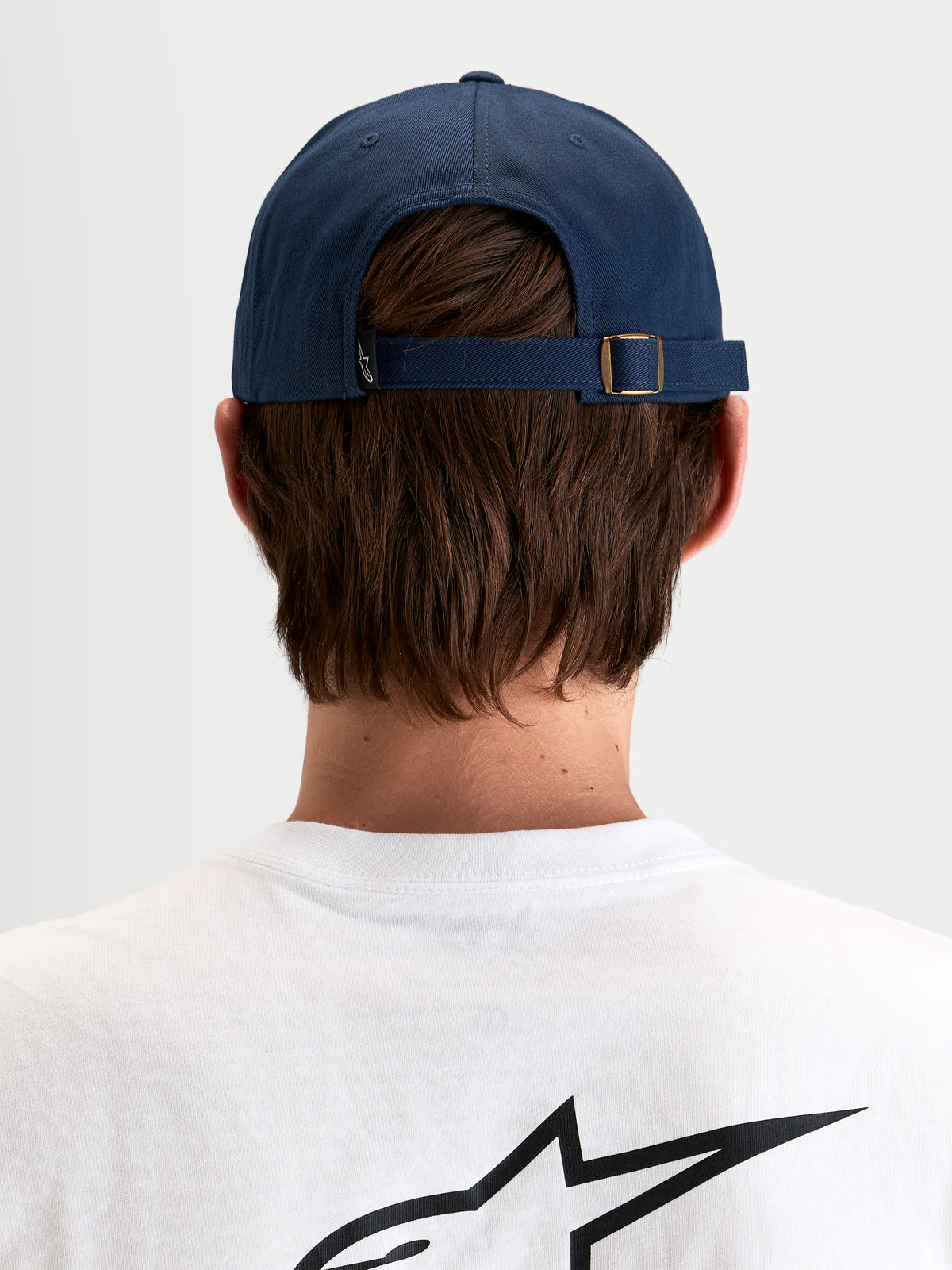 Alpinestars Casquette Dad Dylan, casquette sportswear décontractée en bleu marine, vue de dos montrant la sangle arrière réglable avec boucle en métal et petite étiquette du logo Astars portée par un modèle
