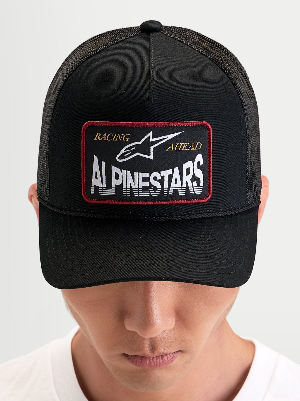 Alpinestars Casquette Trucker Hemmings, casquette snapback sportswear noire portée par un modèle, avec écusson tissé du logo sur le devant et panneaux arrière en mesh respirant