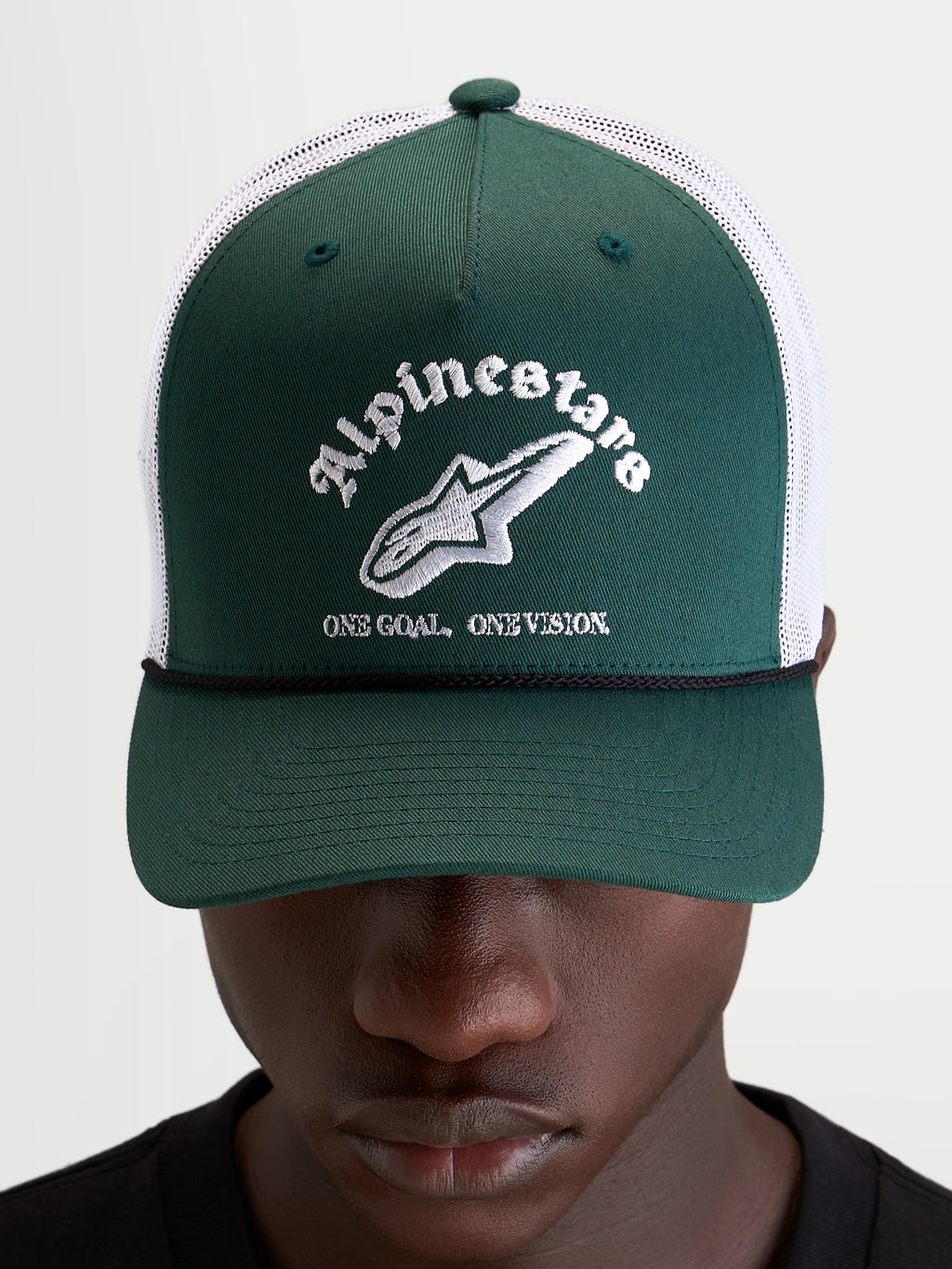 Alpinestars Baron Trucker Hat, casual sportswear cap worn by a model, green and white, featuring a curved bill, structured twill front, breathable poly mesh back, and embroidered Alpinestars word combo logo on the front