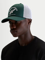 Alpinestars Baron Trucker Hat, casual sportswear cap worn by a model, green and white, featuring a curved bill, structured twill crown, breathable mesh back, and embroidered front logo