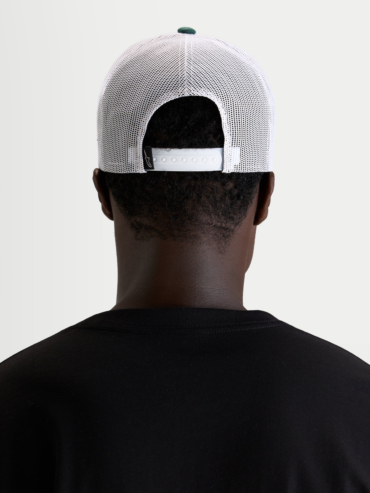 Alpinestars Baron Trucker Hat, casual sportswear mesh cap, worn by a model, rear view showing adjustable snapback closure and white poly mesh panels with green crown button