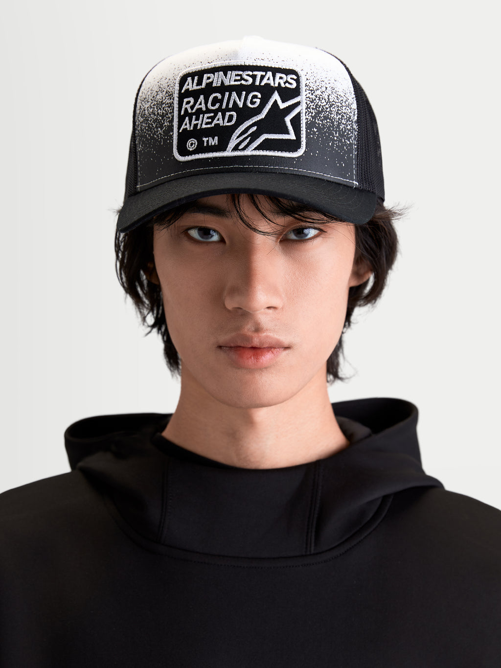 Alpinestars Gravel Trucker Hat, Sportswear Lifestyle Cap, Black and White, On-Model Front View featuring a Curved Bill, Breathable Mesh Back, and Racing Ahead Woven Patch with Gravel Texture Detailing.