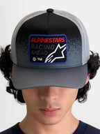 Alpinestars Gravel Trucker Hat, Sportswear Mesh Cap, Dark Gray and Black, featuring a curved bill and a woven front patch with 'Racing Ahead' text and Astars logo, on-model front view.