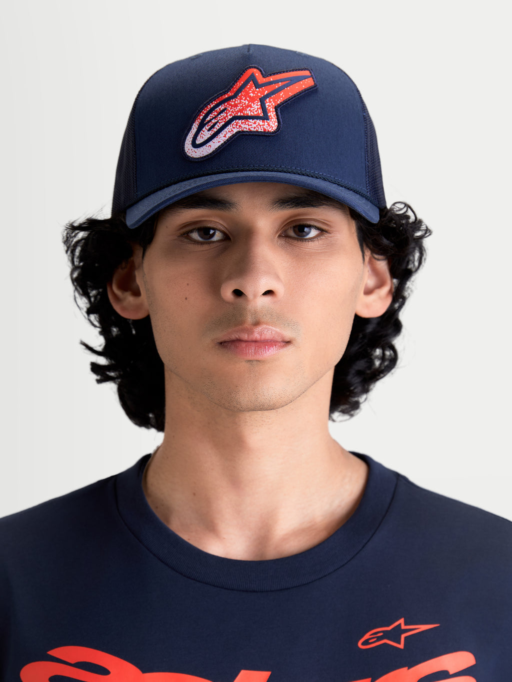 Alpinestars Casquette Trucker Meteorite, casquette sportswear avec arrière en maille pour homme et femme, bleu marine avec logo Astars rouge et blanc à texture gravier, couronne structurée, visière incurvée, vue de face sur un modèle