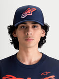 Alpinestars Casquette Trucker Meteorite, casquette sportswear avec arrière en maille pour homme et femme, bleu marine avec logo Astars rouge et blanc à texture gravier, couronne structurée, visière incurvée, vue de face sur un modèle
