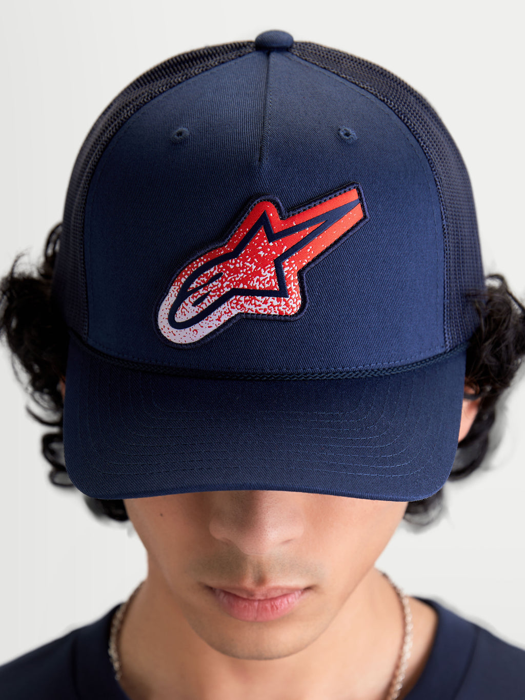 Alpinestars Casquette Trucker Meteorite, casquette de sportswear pour homme et femme, bleu marine avec écusson logo Astars rouge et blanc à texture gravier, couronne structurée et visière incurvée, vue de face portée