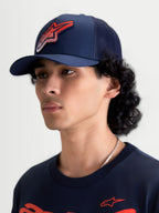 Alpinestars casquette Trucker Meteorite, casquette de sportswear avec arrière en maille, bleu marine et rouge, visière incurvée et couronne structurée, logo Astars à texture gravier, vue portée par un modèle