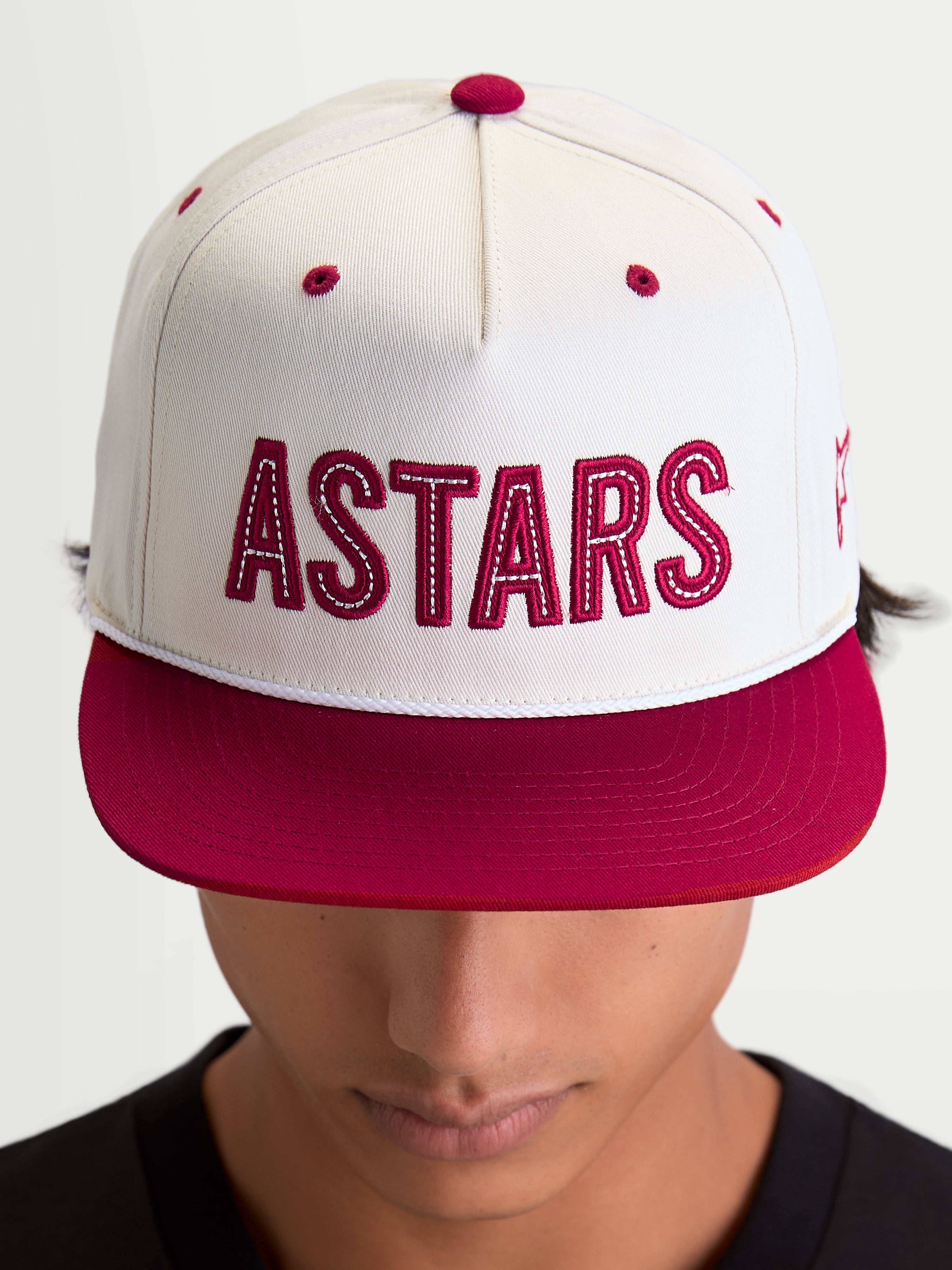 Alpinestars Casquette Stadium Snapback, casquette sportswear à visière plate, blanc cassé et rouge, logo ASTARS en applique avec surpiqûres contrastées, couronne structurée, portée par un modèle.