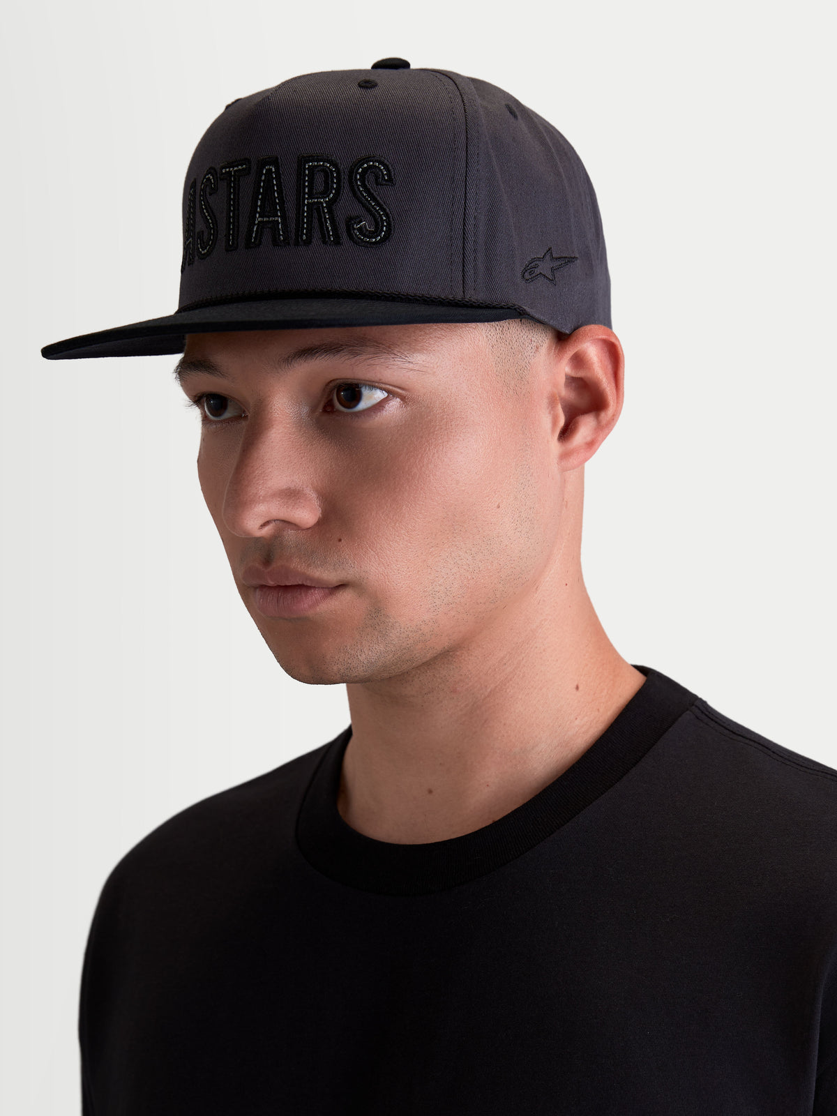 Alpinestars Stadium Snapback Kappe, Motorsport-Sportswear-Kappe für Herren, Dunkelgrau und Schwarz, strukturierte Krone mit flachem Schirm, Astars-Applikation auf der Vorderseite und seitliche Logo-Stickerei, Baumwoll-Twill, Ansicht am Modell.