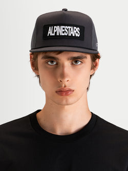Alpinestars Ten Trucker-Kappe, flache Sportswear-Cap in Dunkelgrau, getragen von einem Model, mit strukturierter Krone und vorderem Alpinestars Wortlogo-Stickpatch