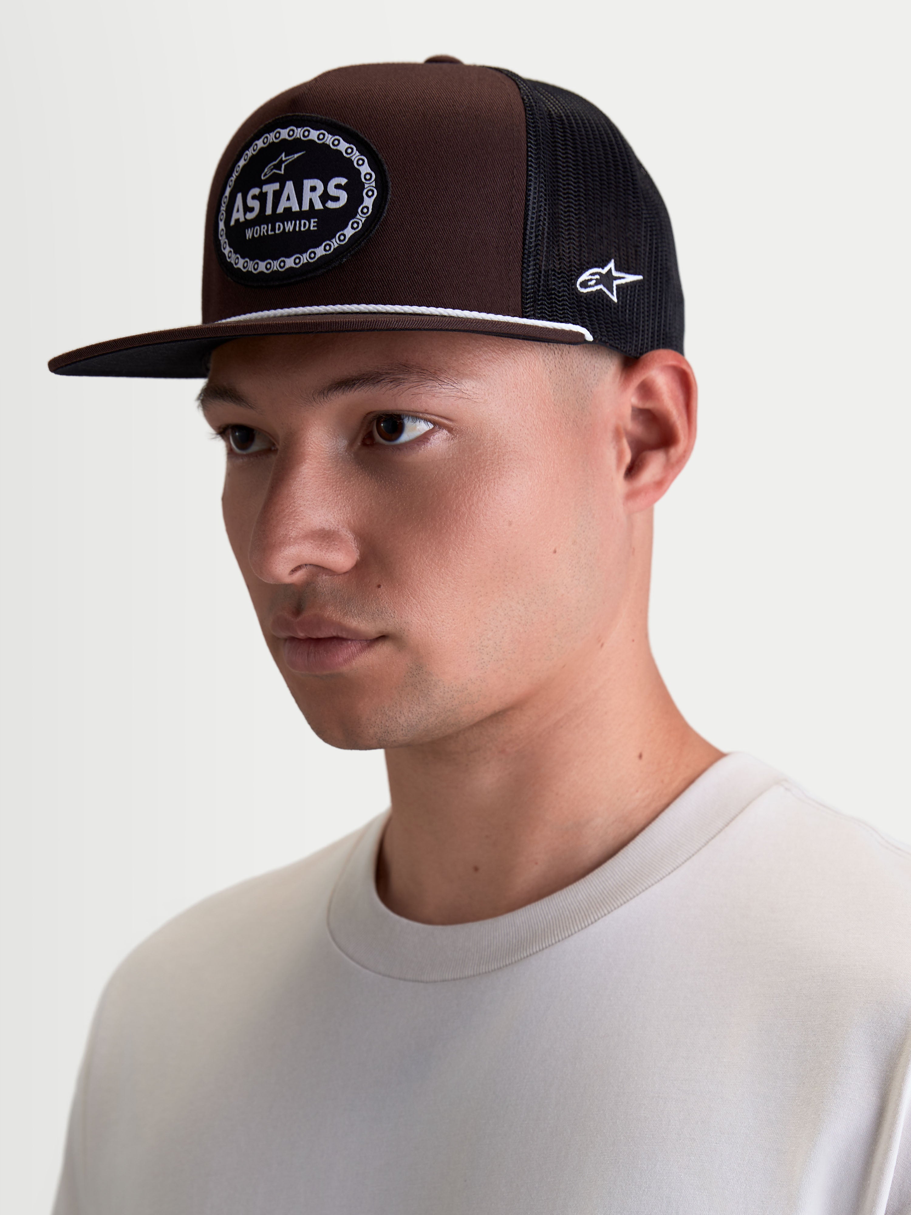 Alpinestars Hotlink Trucker pet op model, bruine en zwarte lifestyle sportswearpet met platte klep, gestructureerde kroon van twill en een geweven Astars-logopatch met fietskettingrand.