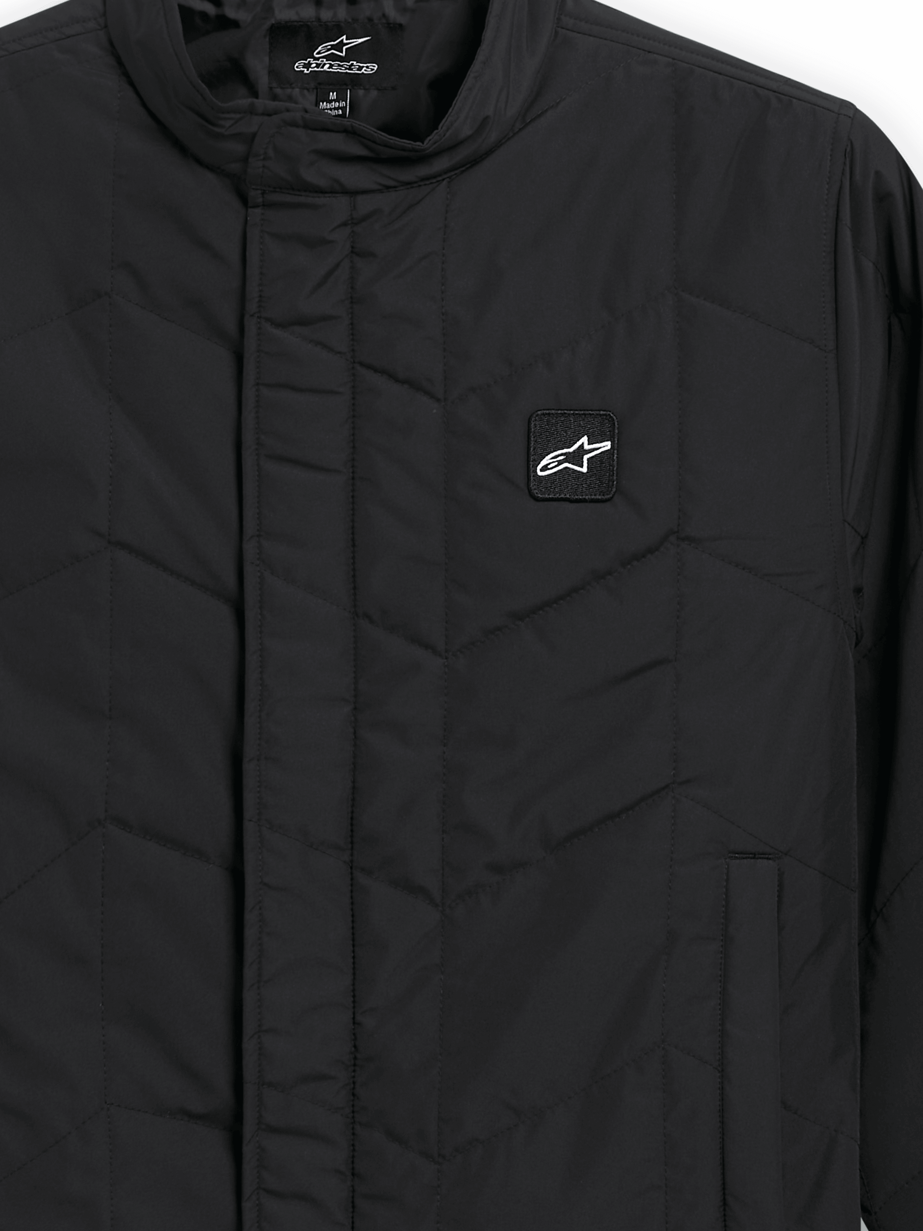 Alpinestars Precedent jas, gestept sportswear jack, zwart, detailopname met een iconisch schuin gestikt patroon, lage kraag, bedekte rits aan de voorzijde en kleine logopatch op de borst