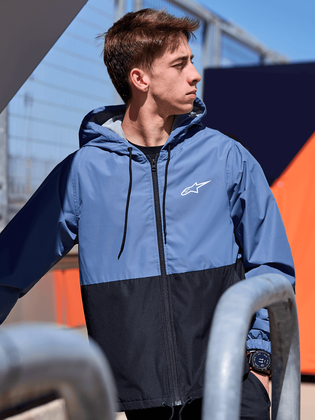 Veste coupe-vent Alpinestars Speeder, coupe-vent léger à capuche, design bicolore bleu ardoise et noir, logo Alpinestars blanc sur la poitrine, doublure en mesh et capuche à cordon de serrage, streetwear décontracté inspiré du sport automobile