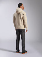 Alpinestars Ageless V3 Hoodie, lässiger Fleece-Kapuzenpullover in Off-White von hinten gezeigt, mit Rippbündchen an Ärmeln und Saum, getragen mit dunkler Slim-Fit-Jeans und schwarzen Alpinestars-Sneakern