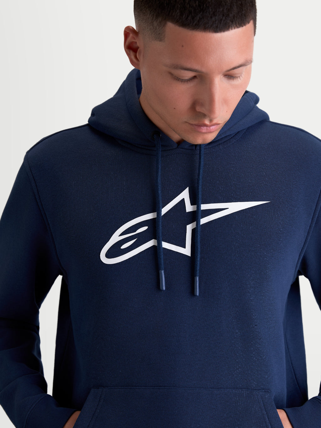 Alpinestars Ageless V3 Hoodie, herensportswear pullover fleece, blauw en wit, met een groot wit geborduurd Alpinestars-logo op de borst, gevoerde capuchon met gedoopte trekkoorduiteinden en zachte fleececonstructie voor casual motorsportlifestyle.