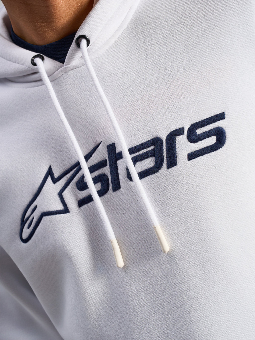 Alpinestars Blaze V3 Hoodie, White Navy, close-up van de borst met donkerblauwe logoprint aan de voorzijde en witte trekkoorden met gedipte uiteinden, casual motorsport streetwear