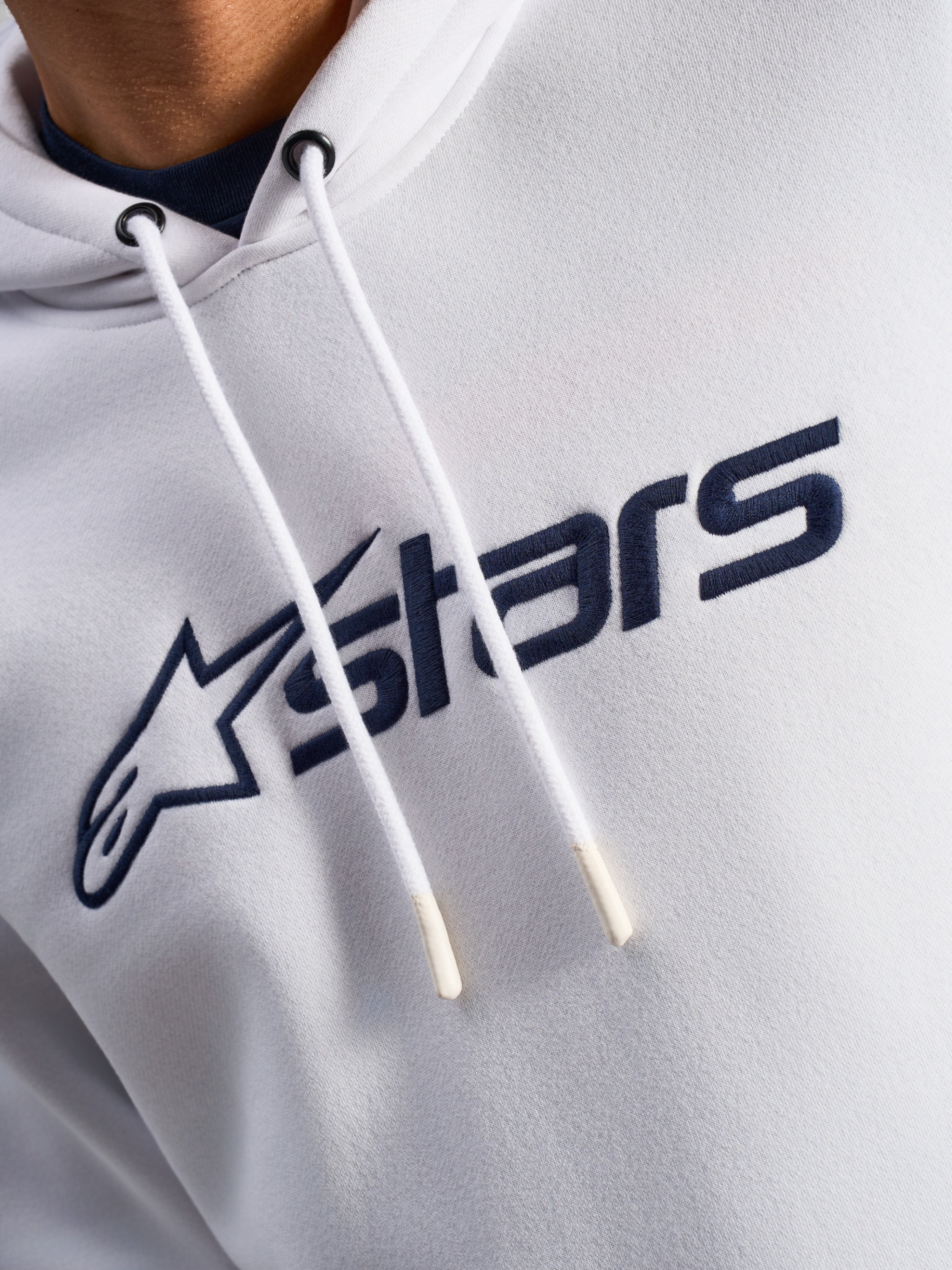 Alpinestars Blaze V3 Hoodie, White Navy, close-up van de borst met donkerblauwe logoprint aan de voorzijde en witte trekkoorden met gedipte uiteinden, casual motorsport streetwear