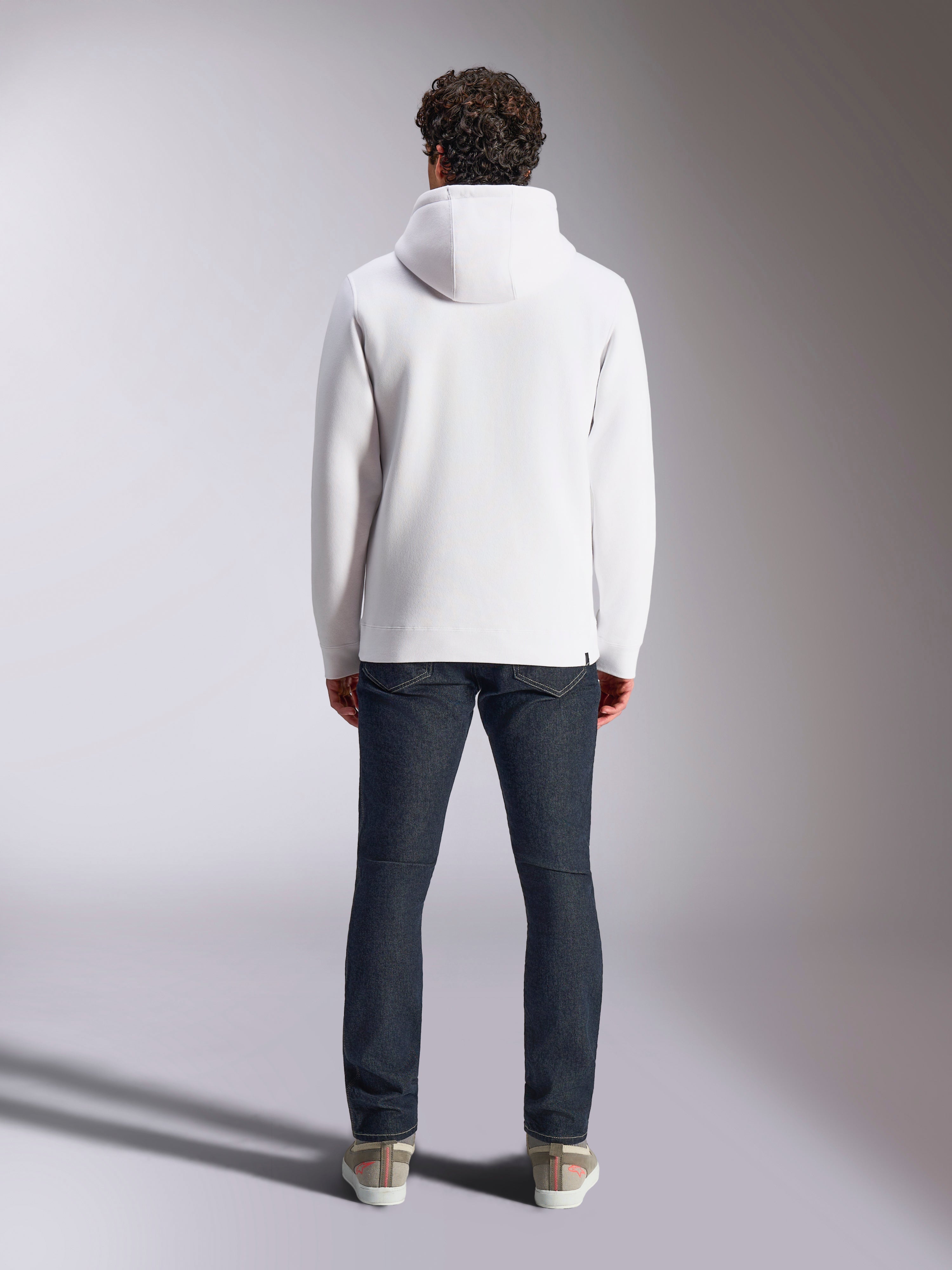 Alpinestars Blaze V3 Hoodie, witte casual sportswear hoodie, achteraanzicht van pullover fleece, strak design met geribbelde manchetten en zoom, gestyled met donkerblauwe jeans en sneakers, moderne motorsport-geïnspireerde lifestyle-kleding
