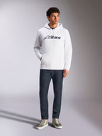 Alpinestars Blaze V3 Hoodie, witte casual streetwear hoodie met navy Alpinestars logo op de borst, gedragen door een model met donkerblauwe jeans en beige sneakers, voorzien van een capuchon met trekkoord en kangoeroezak aan de voorkant