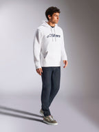 Alpinestars Blaze V3 Hoodie, wit en donkerblauw, casual streetwear gedragen door een model met donkerblauwe jeans en sneakers, voorzien van een capuchon met trekkoord en een opvallende logoprint op de borst, modern op motorsport geïnspireerd design