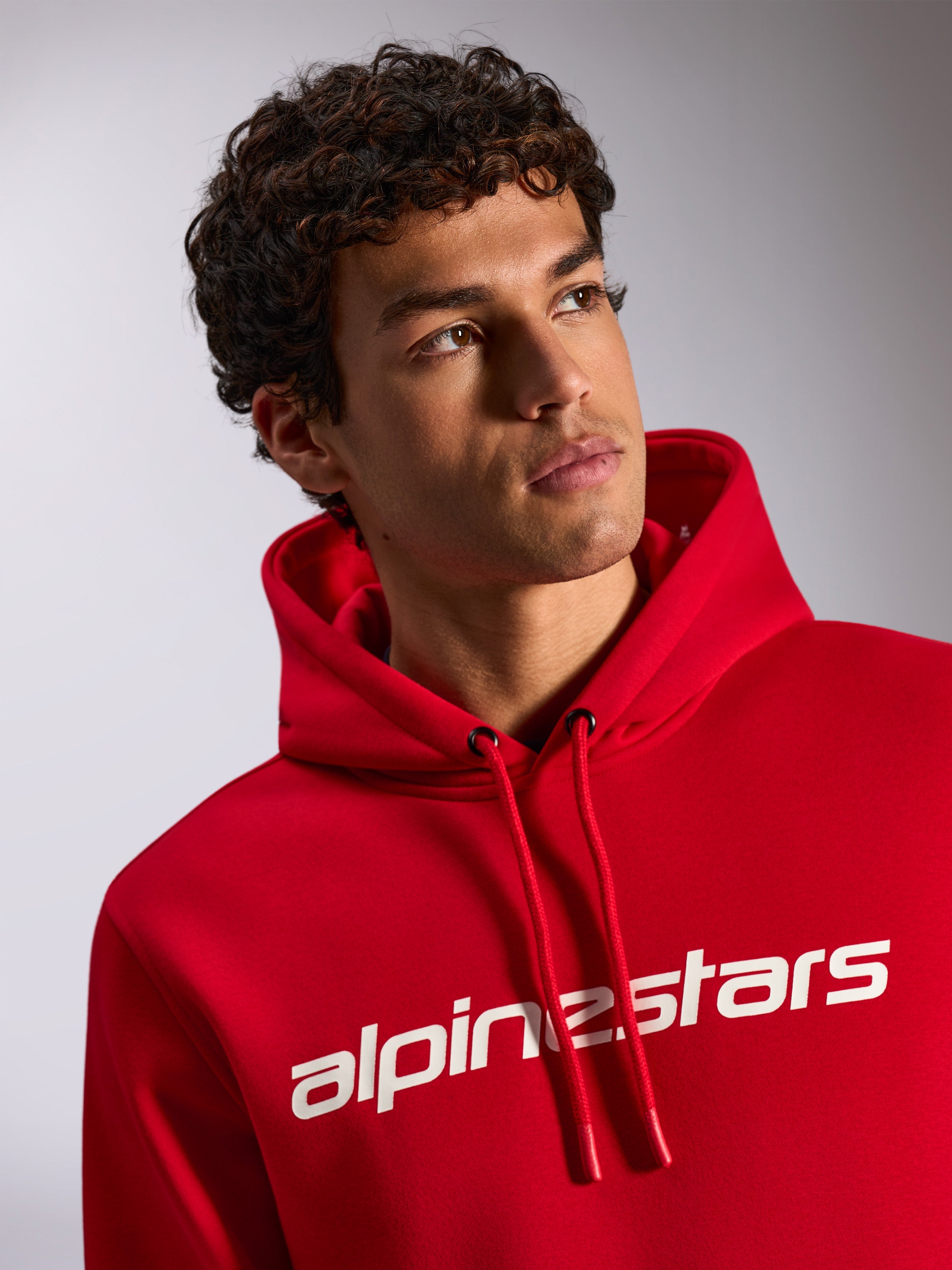 Alpinestars Linear Wordmark V3 Hoodie, rode casual pullover fleece, wit Alpinestars woordmerk op de borst, capuchon met trekkoord en gedipte punten, lifestyle-opname van een mannelijk model