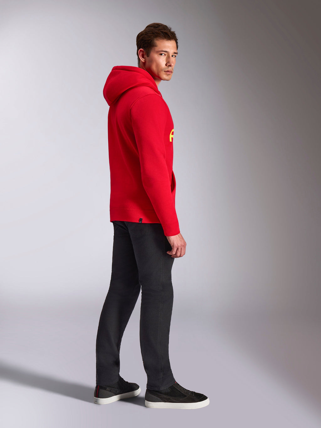 Alpinestars Ride V3 Hoodie, casual sportkleding, rood met Hi-Vis gele branding, mannelijk model draagt rode hoodie met zwarte broek en sneakers, zijaanzicht, pullover fleece ontwerp met geribde manchetten en zoom