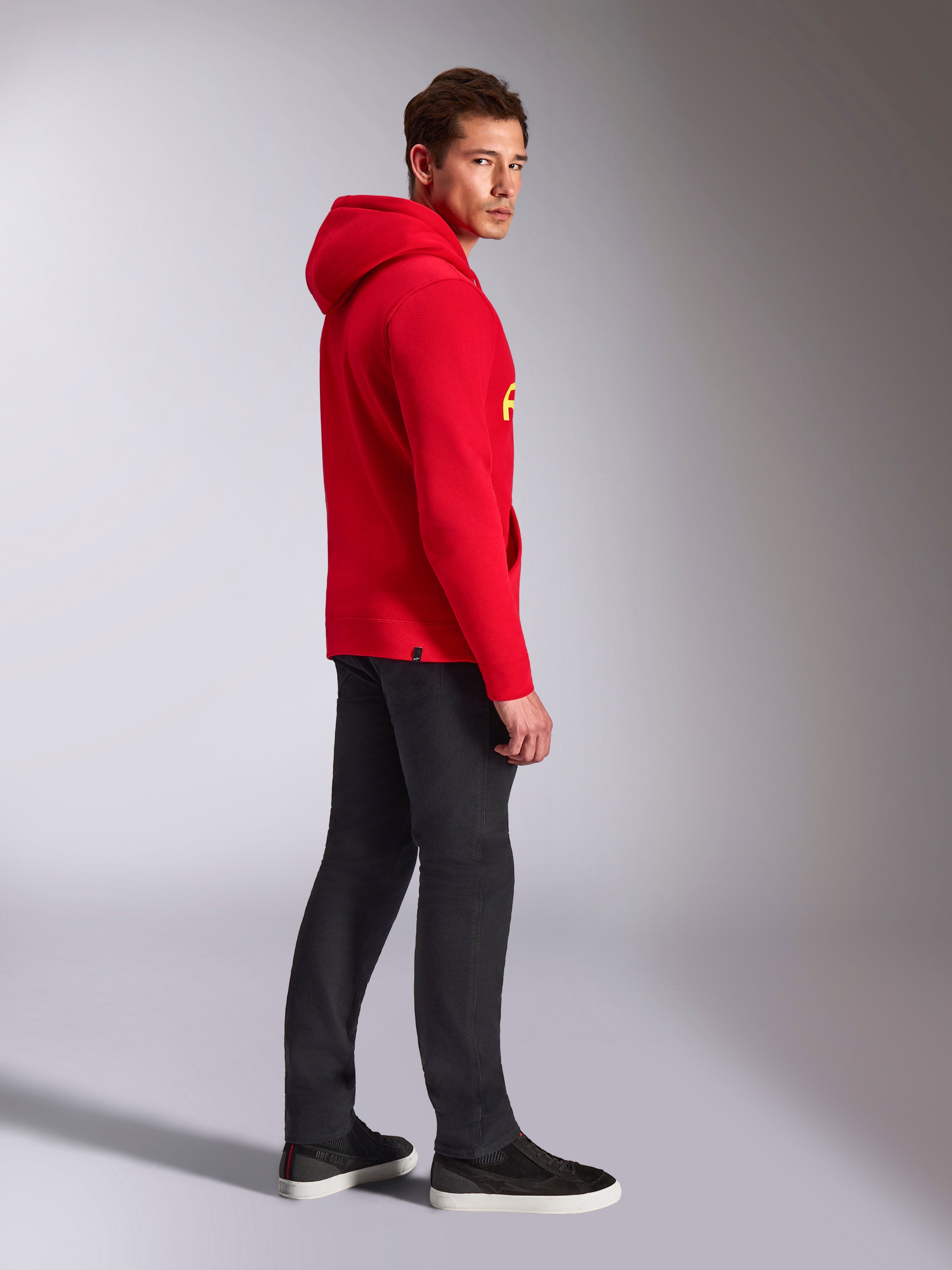 Alpinestars Ride V3 Hoodie, casual sportkleding, rood met Hi-Vis gele branding, mannelijk model draagt rode hoodie met zwarte broek en sneakers, zijaanzicht, pullover fleece ontwerp met geribde manchetten en zoom