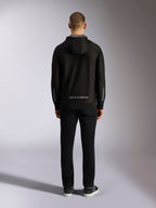 Achteraanzicht van de Alpinestars Sessions V3 Hoodie in Black Grey, met een grijs Alpinestars-woordmerk op de onderrug en Astars-logo's op de onderarmen, gedragen door een model met een zwarte broek, casual motorsport-geïnspireerde streetwear