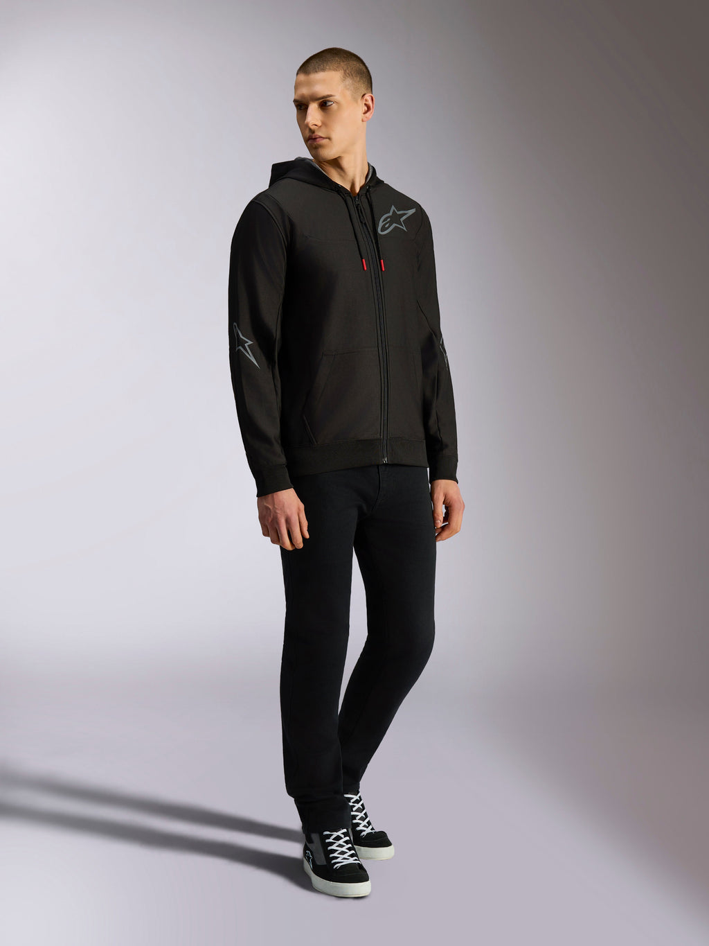 Alpinestars Sessions V3 Hoodie, polyfleece met rits aan de voorkant, zwart en grijs, grijze logo's op de borst en mouwen, capuchon met trekkoord met rode uiteinden, volledige weergave van model in casual motorsport streetwear