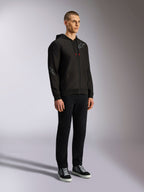 Alpinestars Sessions V3 Hoodie, casual motorsport streetwear, zwarte hoodie met rits en grijs ster-logo op de borst en mouw, trekkoorden met rode uiteinden, geribde manchetten en zoom, gedragen door model met zwarte broek en sneakers.
