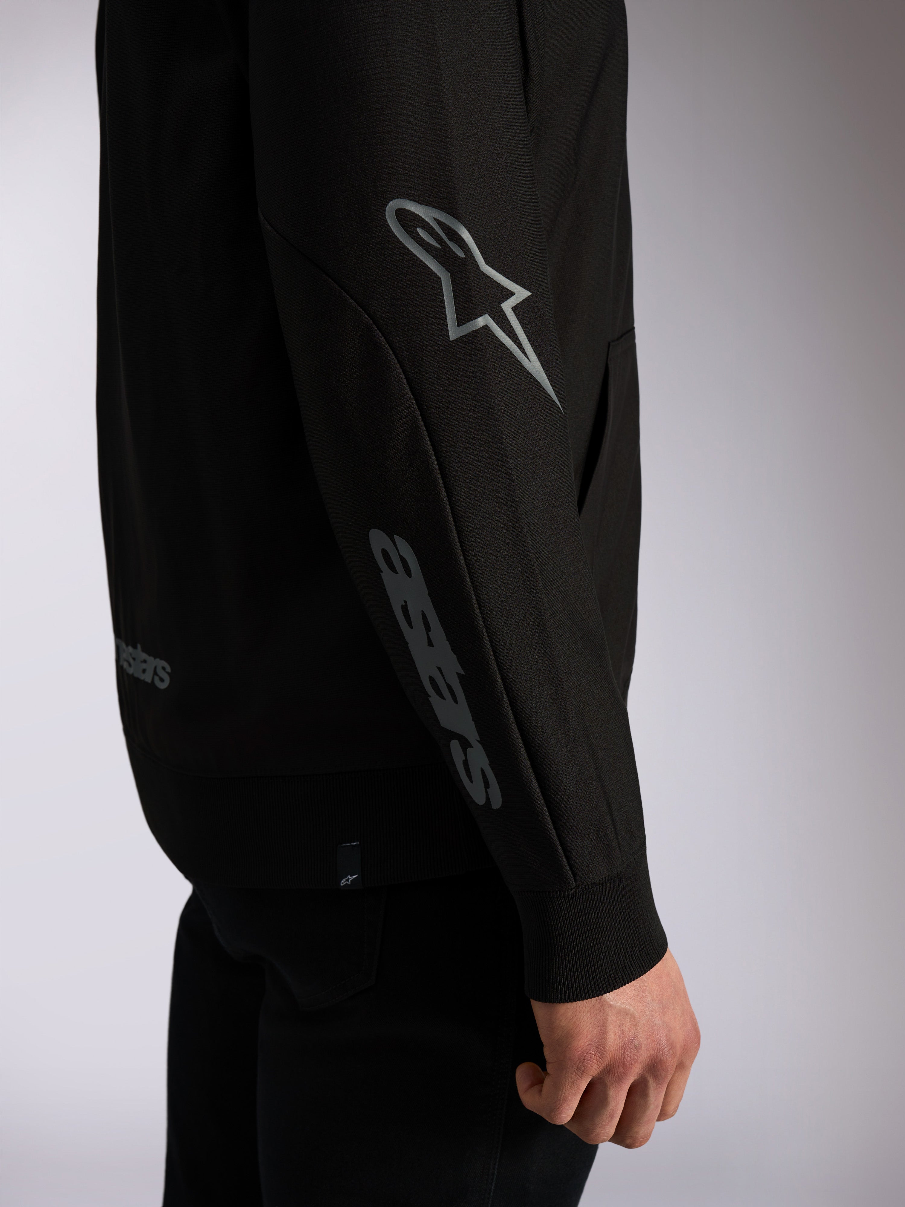 Alpinestars Sessions V3 Hoodie, zwarte casual streetwear, close-up van mouw met grijs Astars-logo op elleboog en woordmerk op onderarm, geribde manchetten, motorsport-geïnspireerd ontwerp