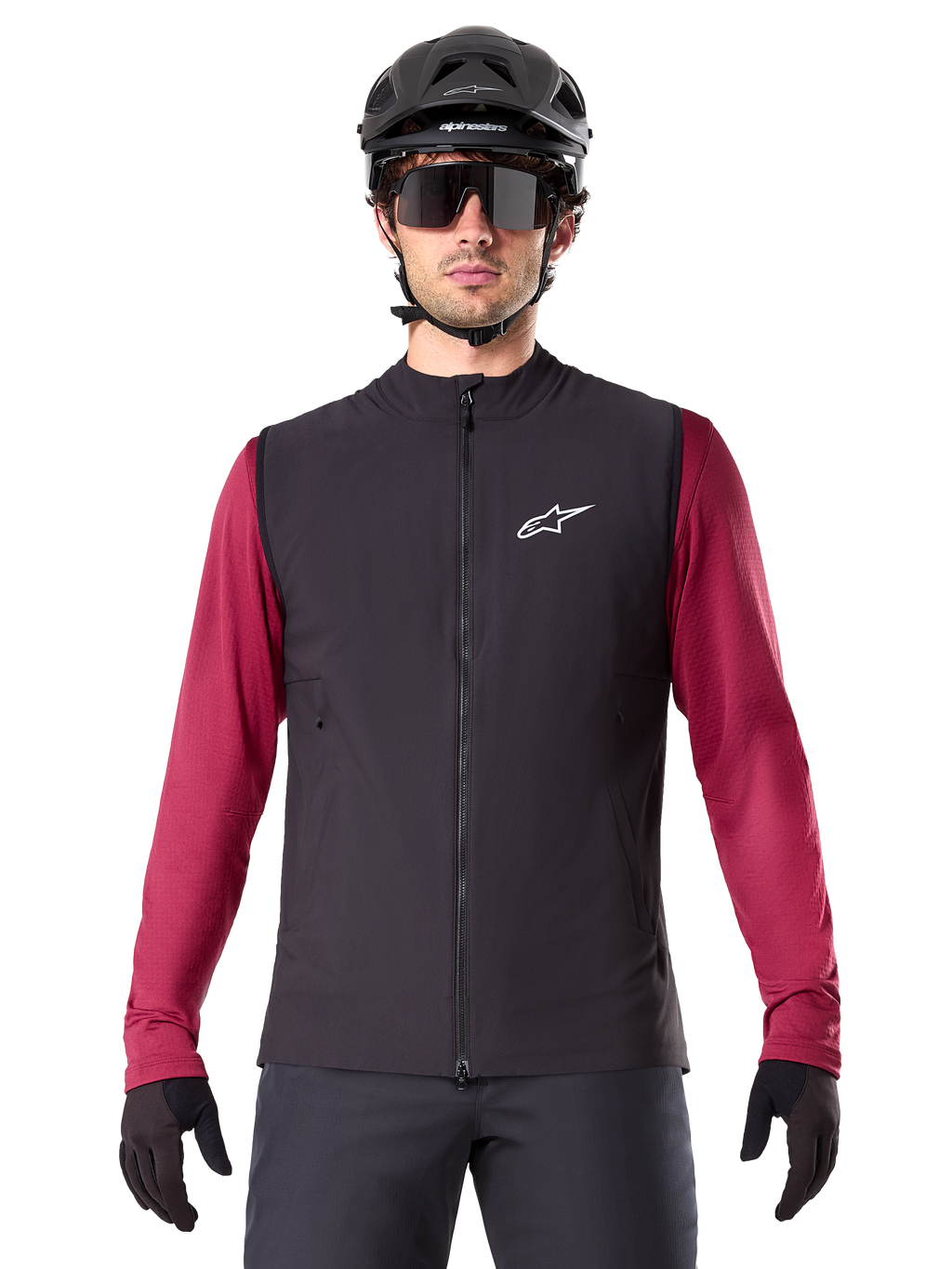 Gilet thermique Alpinestars A-Dura, gilet de cyclisme noir isolé, porté par un mannequin avec un maillot à manches longues bordeaux, casque de VTT noir et lunettes de soleil, avec logo blanc sur la poitrine, protection thermique légère pour le VTT