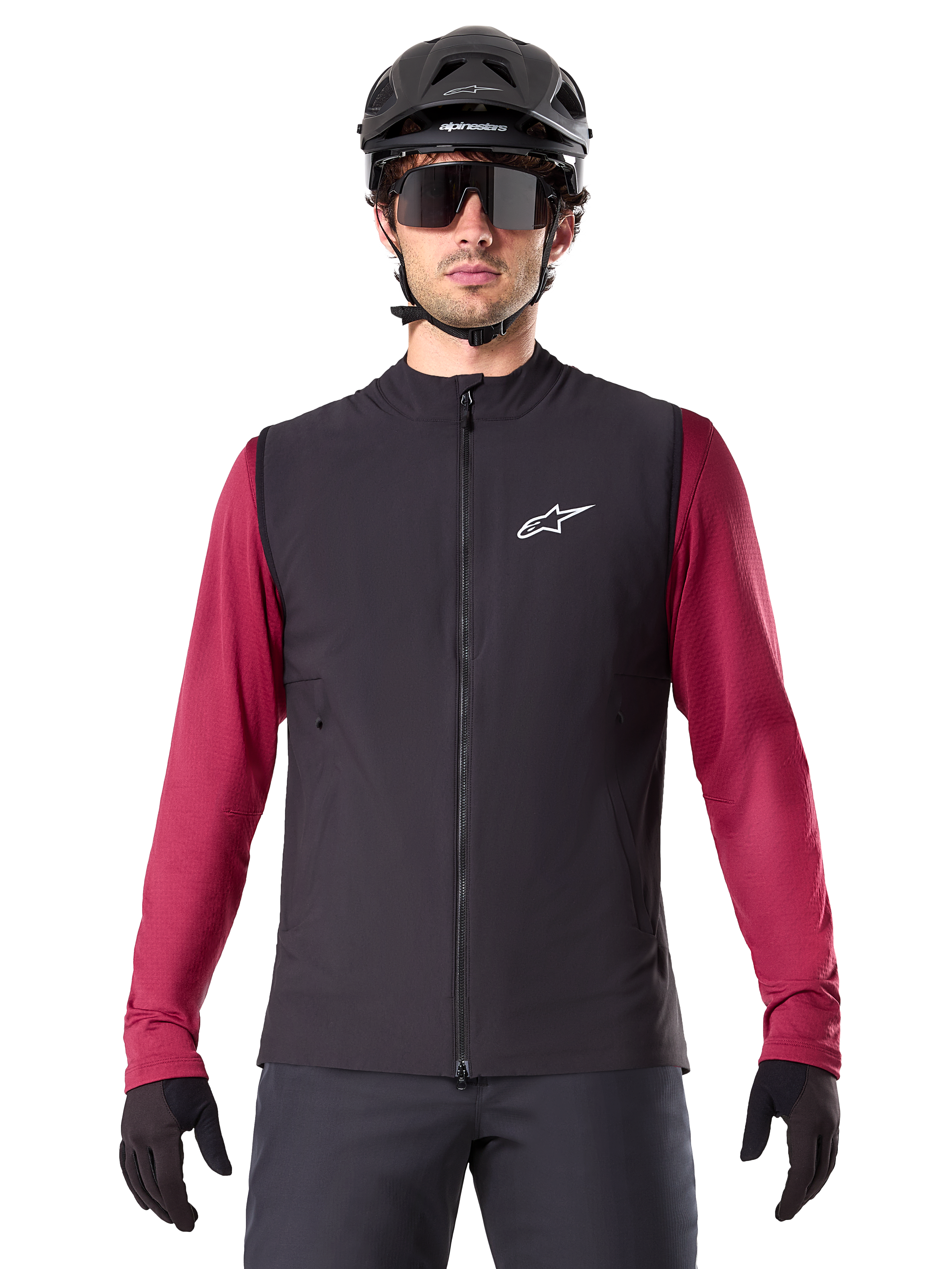 Gilet thermique Alpinestars A-Dura, gilet de cyclisme noir isolé, porté par un mannequin avec un maillot à manches longues bordeaux, casque de VTT noir et lunettes de soleil, avec logo blanc sur la poitrine, protection thermique légère pour le VTT