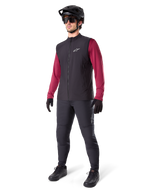 Gilet thermique Alpinestars A-Dura, gilet de cyclisme noir, porté par un cycliste par-dessus un maillot à manches longues bordeaux et un pantalon noir, avec un casque de VTT noir et des gants, conçu pour le VTT par temps froid
