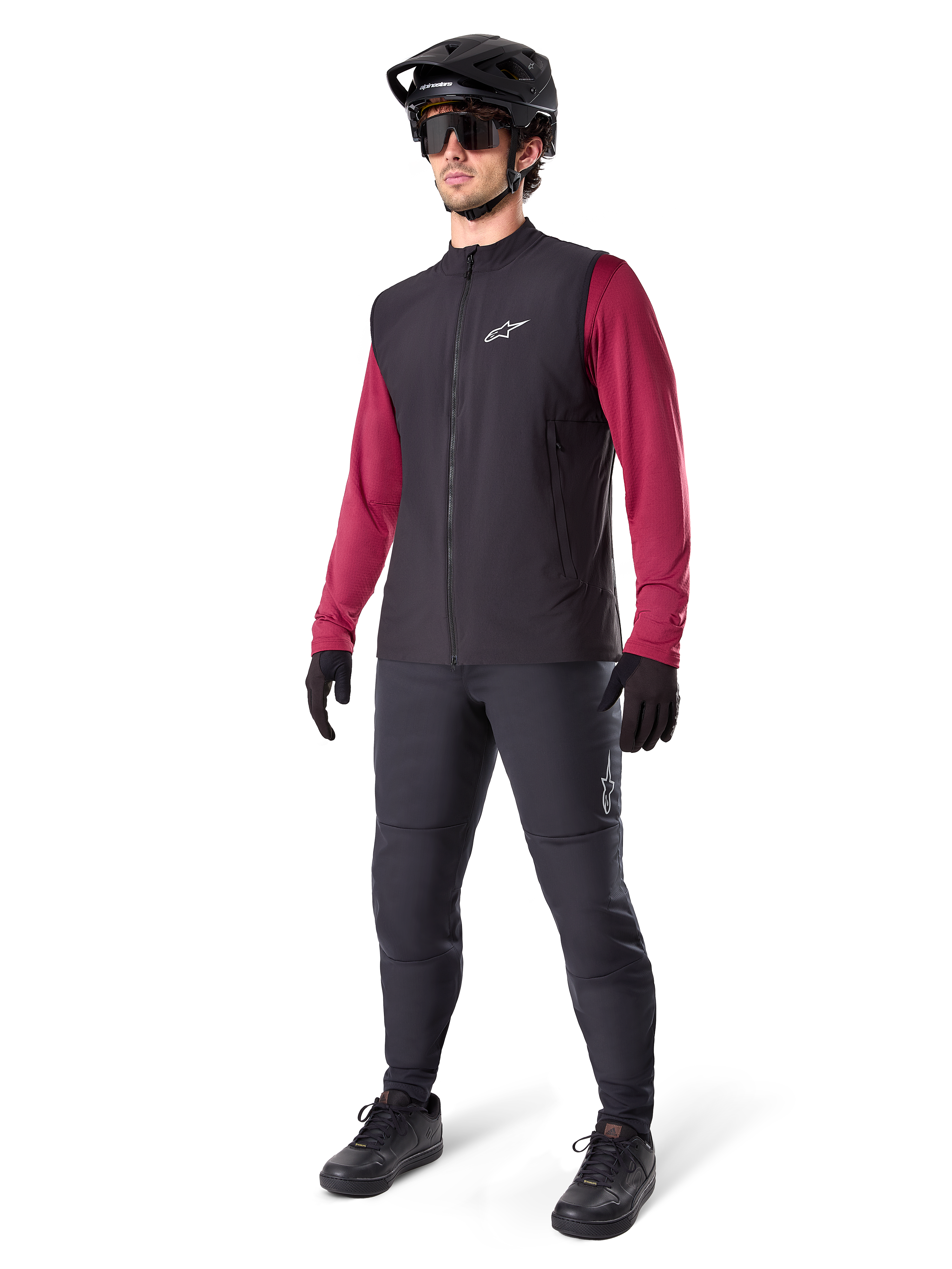 Gilet thermique Alpinestars A-Dura, gilet de cyclisme noir, porté par un cycliste par-dessus un maillot à manches longues bordeaux et un pantalon noir, avec un casque de VTT noir et des gants, conçu pour le VTT par temps froid