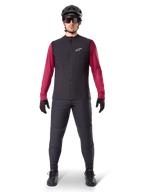 Gilet thermique Alpinestars A-Dura, gilet de cyclisme noir porté sur un maillot à manches longues bordeaux, associé à un pantalon de VTT gris foncé, casque et lunettes de soleil noirs, vêtement technique de VTT pour rouler par temps froid