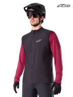Alpinestars A-Dura Thermal Vest, men's mountain biking thermal vest in black, worn by a model with a helmet and a red long-sleeve jersey, insulation for cold-weather MTB riding