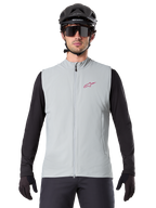 Gilet thermique Alpinestars A-Dura, gilet de cyclisme, gris Titanium, porté avec un maillot noir à manches longues et un casque de cyclisme noir, logo étoile Alpinestars rouge sur la poitrine, léger et isolé pour le VTT